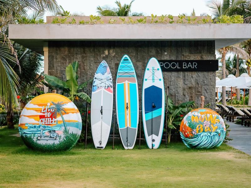 Cztery kolorowe deski surfingowe i dwie kolorowe piłki stoją obok znaku baru przy basenie na zielonej trawie.