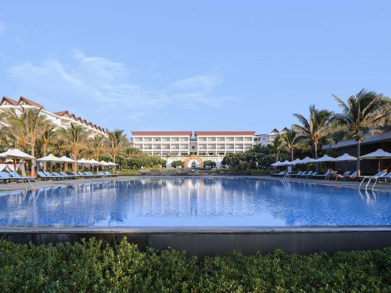 Duży basen hotelowy z leżakami i palmami pod niebieskim niebem