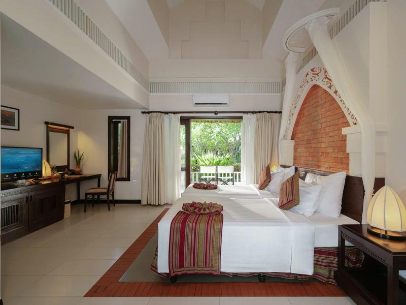 Jasny pokój hotelowy z podwójnym łóżkiem, biurkiem, krzesłem i tarasem z widokiem na ogród.