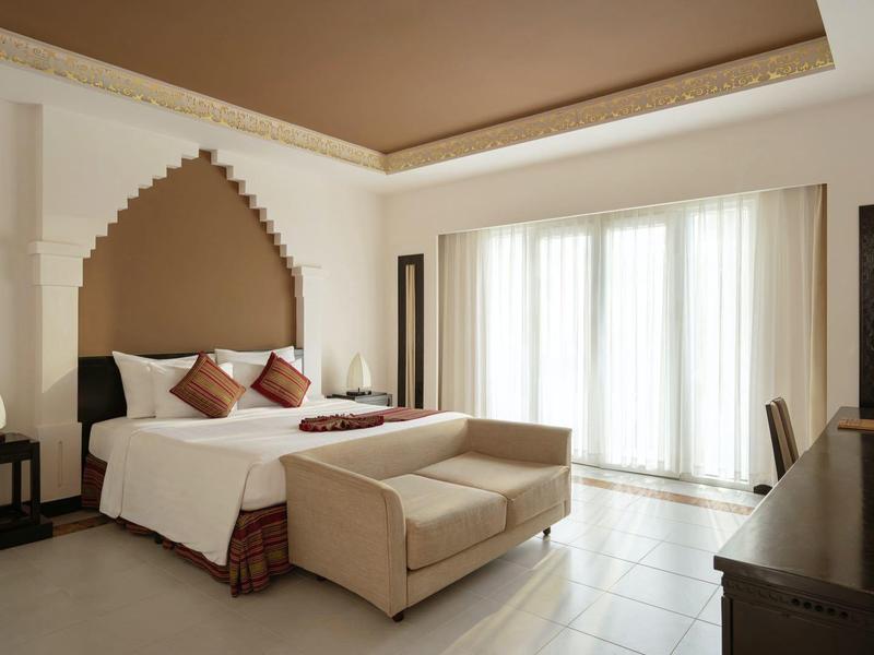 Elegancki pokój hotelowy z dużym łóżkiem, sofą, biurkiem i dużymi oknami z białymi zasłonami