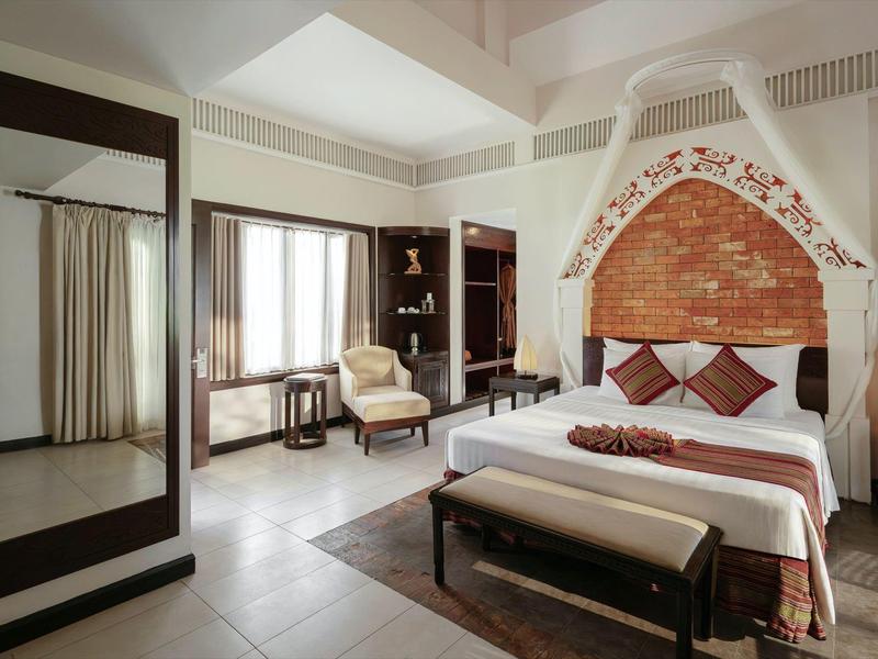 Jasny pokój hotelowy z łóżkiem podwójnym, miejscem do siedzenia, dużym lustrem i oknem z zasłonami.