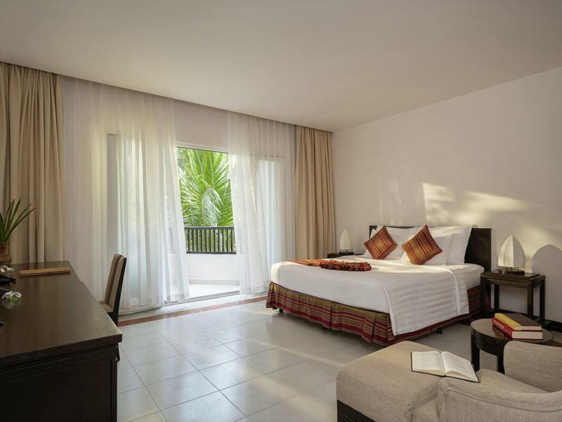 Jasny pokój hotelowy z podwójnym łóżkiem, widokiem na balkon i prostym nowoczesnym wyposażeniem.