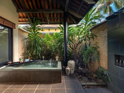 Zadaszony teren na zewnątrz z jacuzzi, roślinami i rustykalną podłogą.