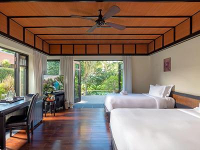 Jasny pokój hotelowy z dwoma łóżkami, drewnianą podłogą i widokiem na ogród.