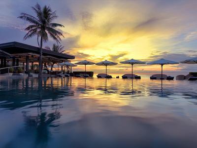 Zachód słońca przy basenie z cieniami parasoli i palm w ośrodku.