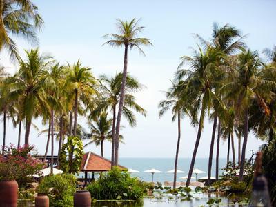 Tropikalny obszar hotelowy z palmami, basenem i widokiem na morze pod bezchmurnym niebem.