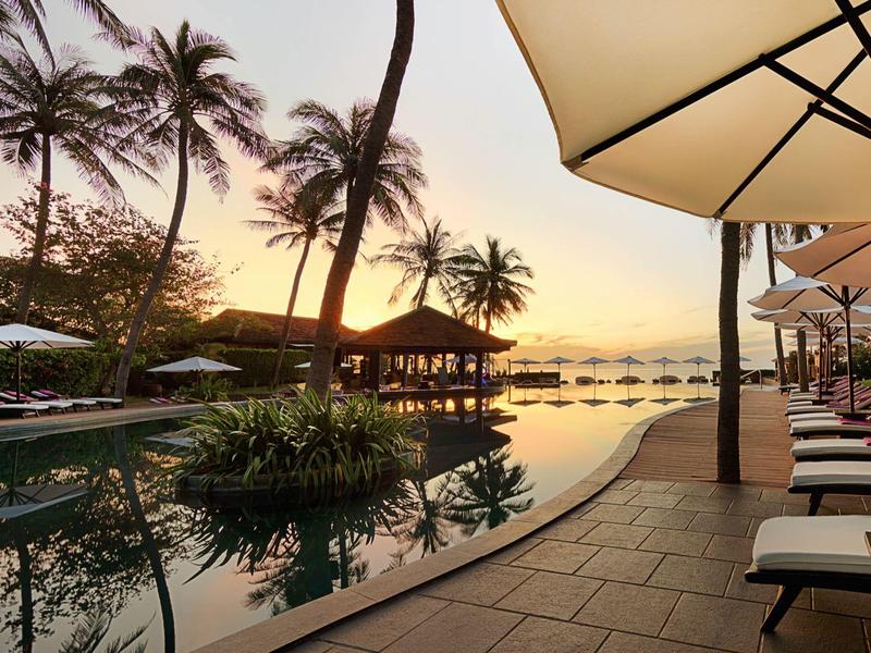 Widok na basen z leżakami i palmami o zachodzie słońca w hotelu