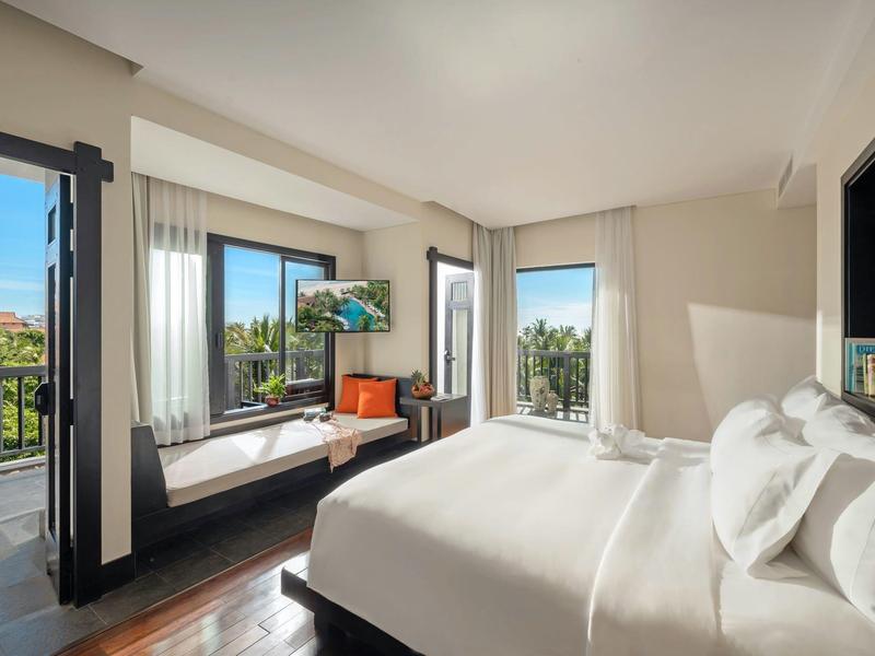 Jasny pokój hotelowy z łóżkiem king-size, siedziskiem przy oknie i widokiem na zielony krajobraz.