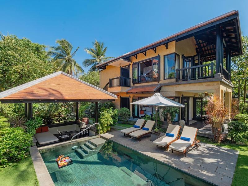 Nowoczesny dwupiętrowy bungalow z basenem, leżakami i zadaszonym miejscem do siedzenia w tropikalnym ogrodzie.