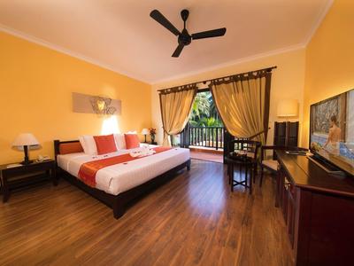 Chambre d'hôtel lumineuse avec sol en bois, lit double, ventilateur de plafond et vue sur balcon.