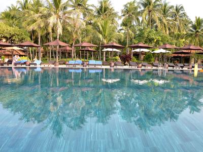 Velký bazén s lehátky a slunečníky obklopený palmami v resortu.