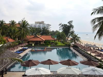 Velký bazén s lehátky a palmami u pláže pod zataženou oblohou.