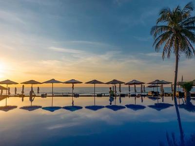 Infinity bazén s slunečníky a palmami při západu slunce u moře