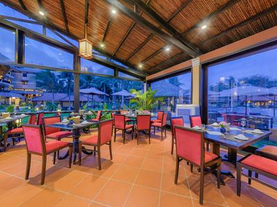 Restaurant en plein air avec chaises rouges et toit en bois le soir près de l'eau.