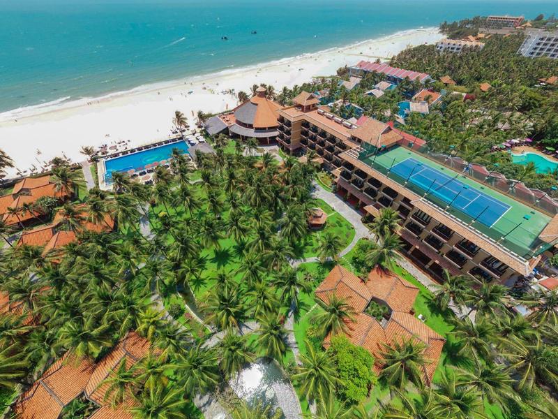 Complex hôtelier avec palmiers, piscines et plage au bord de la mer turquoise.