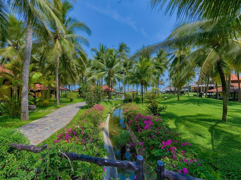 Jardin tropical de station avec palmiers, fleurs et sentiers sous un ciel bleu.