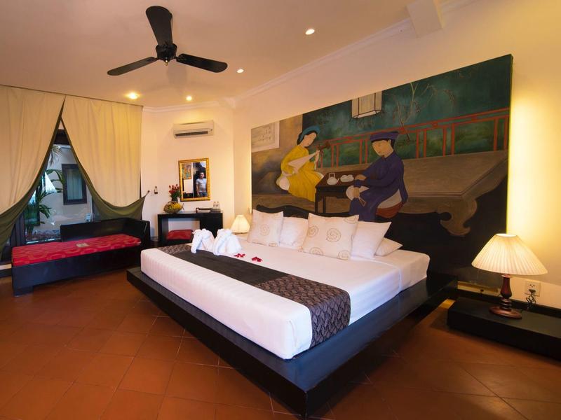 Chambre d'hôtel moderne avec grand lit, ventilateur au plafond, peinture murale artistique et coin salon confortable.