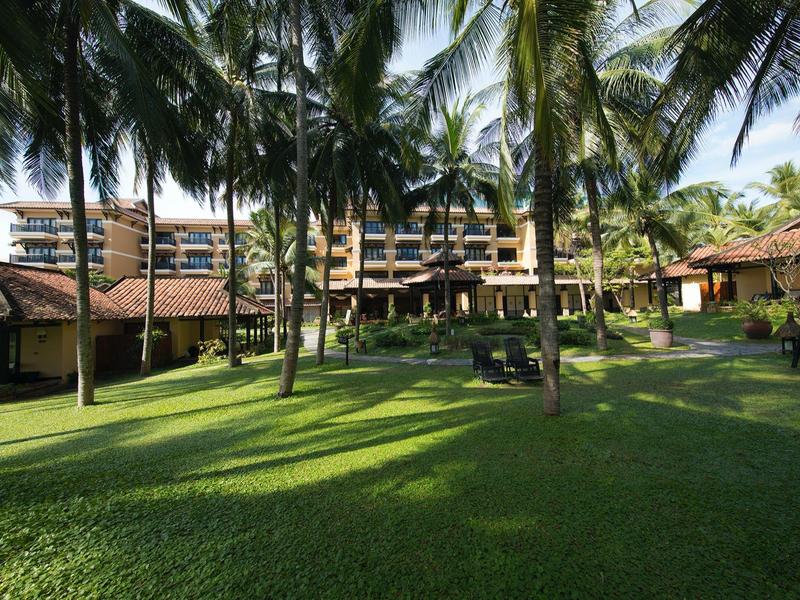 Grand hôtel avec pelouse verte et grands palmiers sous un ciel bleu.