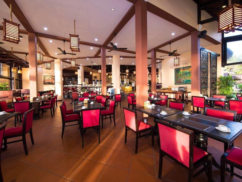 Grand restaurant d'hôtel avec chaises rouges, tables en bois et éclairage chaleureux.