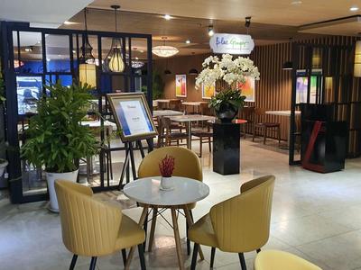 Moderner, heller Raum mit runden Tischen, gelben Stühlen, Pflanzen und dekorativen Elementen im Hintergrund.