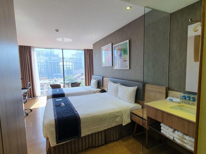 Modernes Hotelzimmer mit großem Fenster, Doppelbett, Schreibtisch und hellen Holzmöbeln.