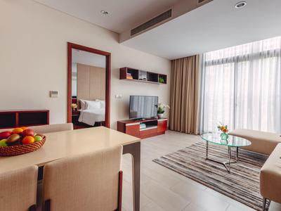 Heller Wohnraum mit Sofa, Teppich, Glastisch, TV an Wand und Esstisch mit Obstschale.