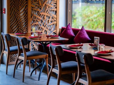 Modernes Restaurant mit Holztischen und Stühlen, dekorativem Wandmuster und roten Kissen.