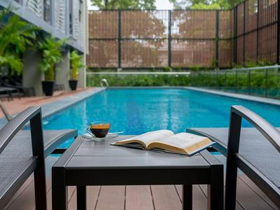 Blauer Pool mit schwarzen Liegestühlen, kleinem Tisch, Buch und Getränk auf Holzdeck.