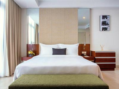 Modernes Schlafzimmer mit großem Bett, weißer Bettwäsche, zwei Nachttischen und grünem Hocker vorne.