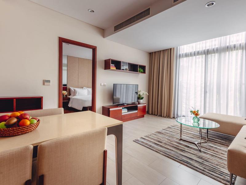 Heller Wohnraum mit Sofa, Teppich, Glastisch, TV an Wand und Esstisch mit Obstschale.