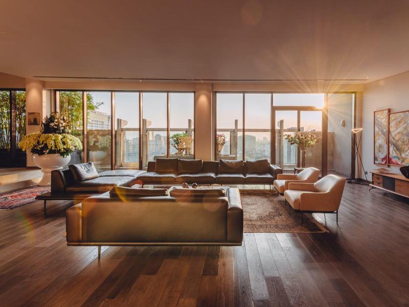 Großes Wohnzimmer mit Holzfußboden, großen Fenstern, Ledersofas und moderner Dekoration bei Sonnenlicht.