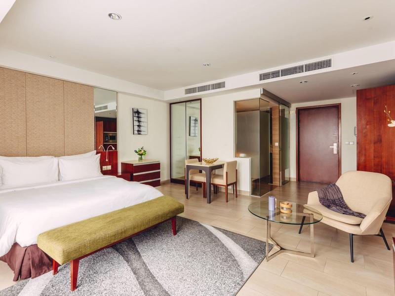 Helles Hotelzimmer mit großem Bett, Sitzbank, Schreibtisch, Sessel und modernem Holzdekor.