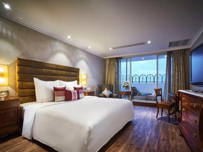 Modernes Hotelzimmer mit großem Bett, Holzmöbeln und Balkon mit Meerblick.