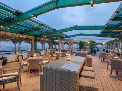 Terrasse mit Glasdach, Holzfußboden, Korbstühlen und Blick auf Gewässer bei Abenddämmerung.