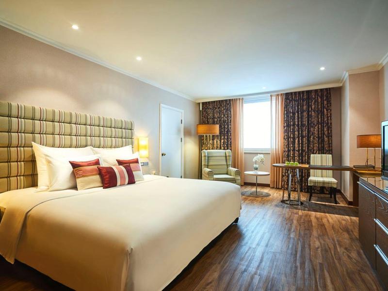 Helles, modernes Schlafzimmer mit großem Bett, Holzboden, Fenster und Fernseher auf Kommode.