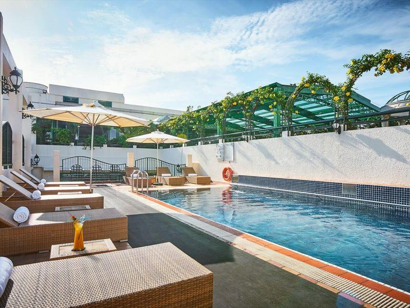 Moderner Außenpool mit Liegen, Sonnenschirmen und weißen Wänden unter blauem Himmel.