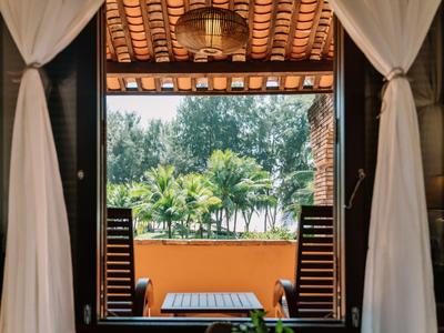 Uitzicht door een open raam met witte gordijnen op een terras en palmbomen op de achtergrond.