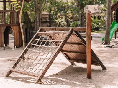 Structure d'escalade en bois et corde dans une aire de jeux sablonneuse en plein air.