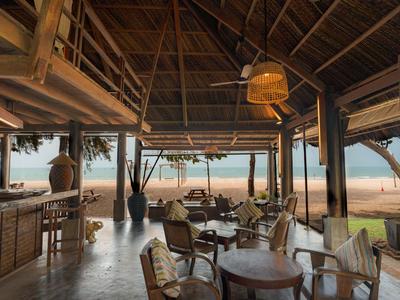 Open restaurant met houten meubels en uitzicht op een zandstrand en de zee.