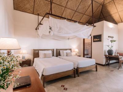 Moderne hotelkamer met twee eenpersoonsbedden, houten meubels en decoratief muskietennet aan het plafond.