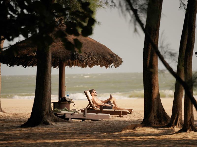 Plage avec chaises longues sous des toits de chaume face à la mer calme.