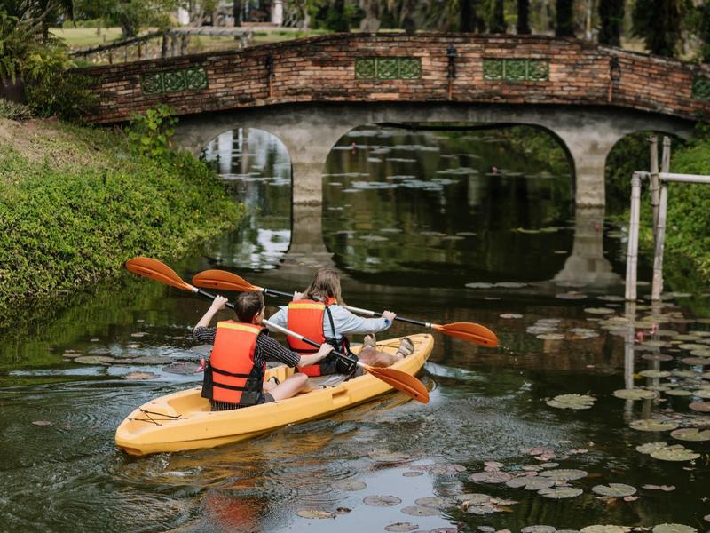Deux personnes dans un kayak jaune sur un cours d'eau sous un pont en pierre.
