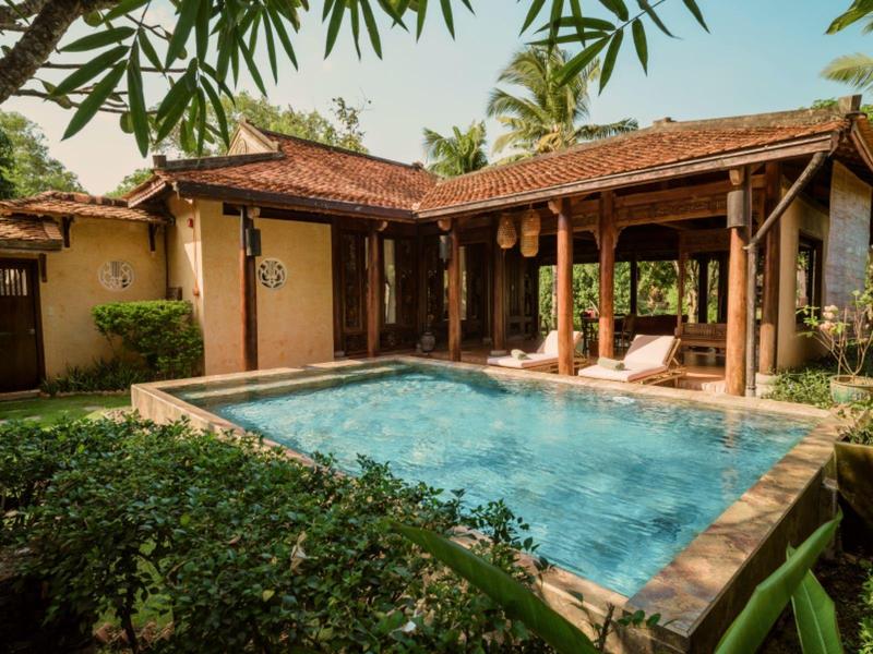 Maison de vacances confortable avec piscine, entourée de palmiers et de verdure luxuriante.