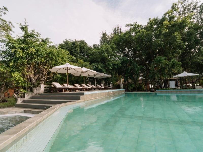 Piscine claire avec chaises longues et parasols entourée d'arbres verts.