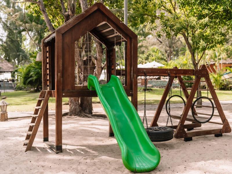 Aire de jeux pour enfants avec toboggan vert, maison en bois et balançoire en plein air.