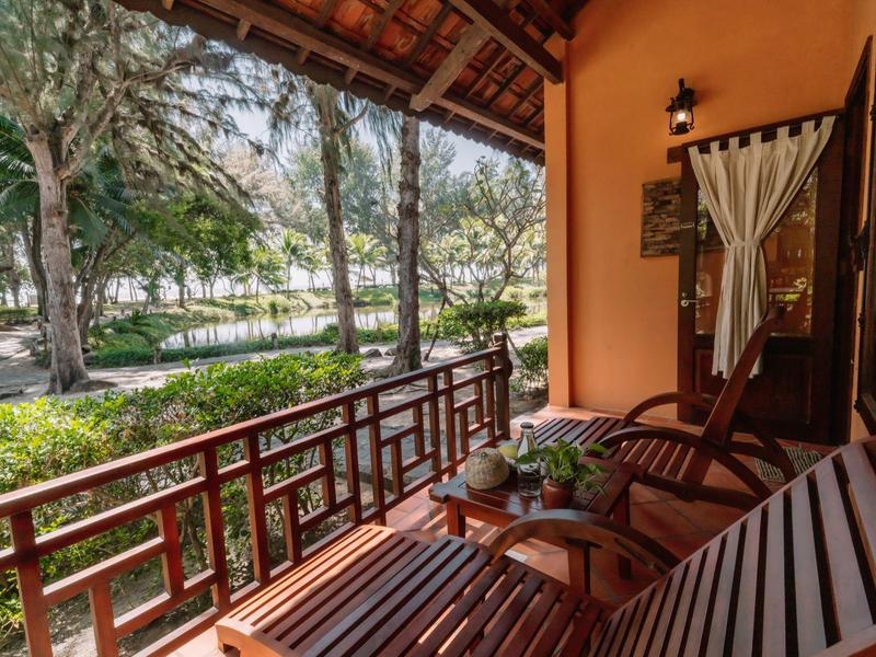 Balcon en bois avec sièges et vue sur un jardin vert avec des arbres.