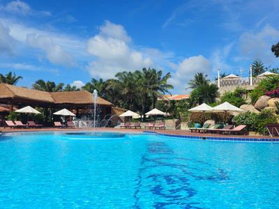 Gran piscina exterior con agua azul, rodeada de sombrillas y palmeras en un día soleado.