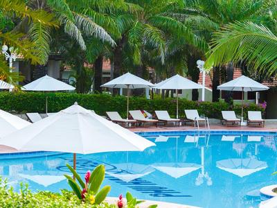 Schwimmbecken mit weißen Sonnenschirmen, Liegen und grünen Palmen im Hintergrund.