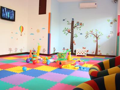 Área de juegos colorida con colchonetas, decoraciones de pared y juguetes para niños en un hotel.
