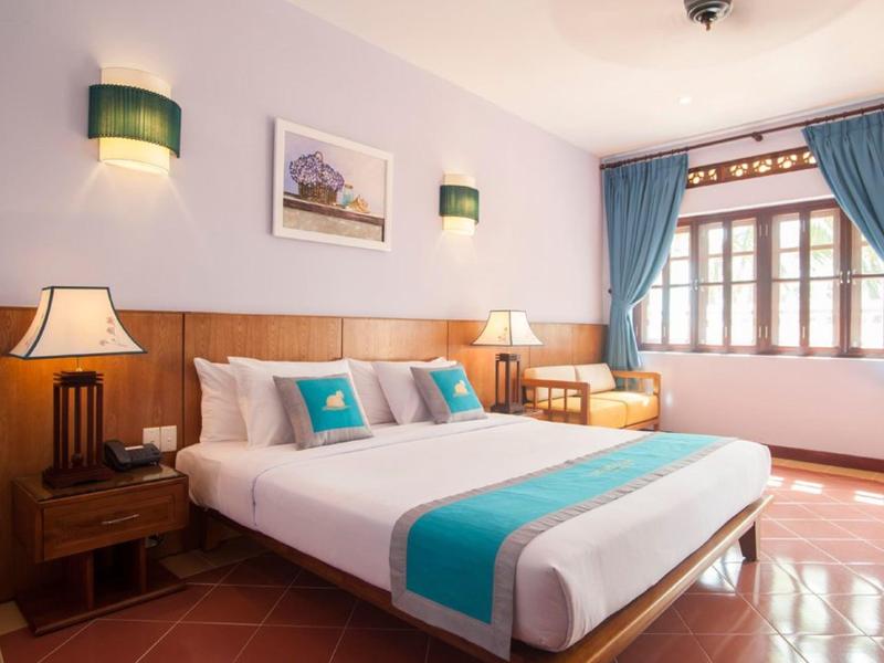 Habitación de hotel acogedora con cama doble, detalles en azul y ventana grande con cortinas.